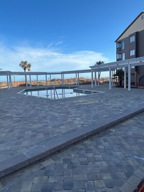 Uma área de piscina com pérgola, um edifício com varandas e vista para a praia.