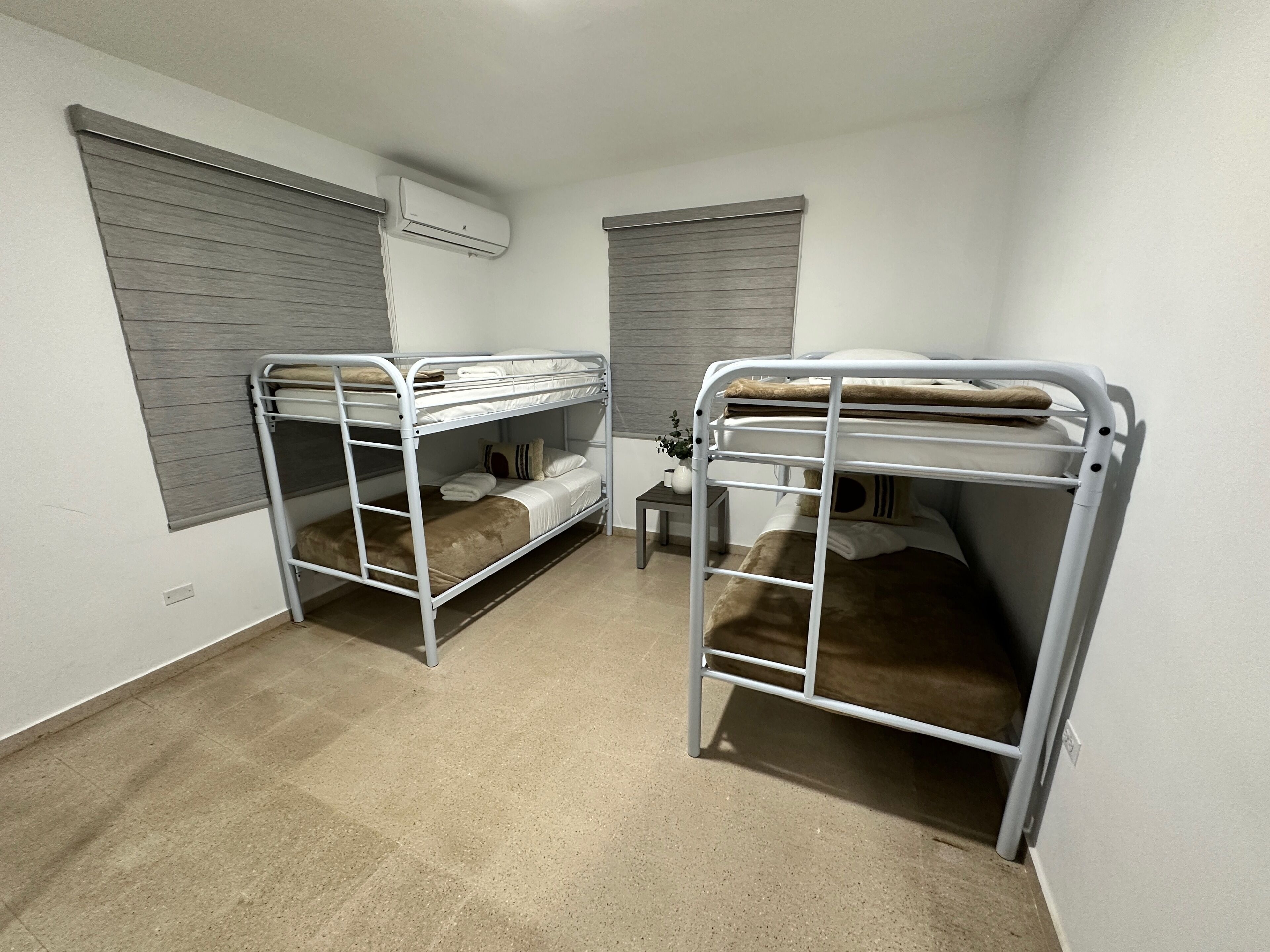 A room with two bunk beds, a small table, and a potted plant.