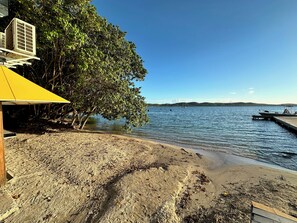 A beach with a yellow structure, a dock, and boats in the water.