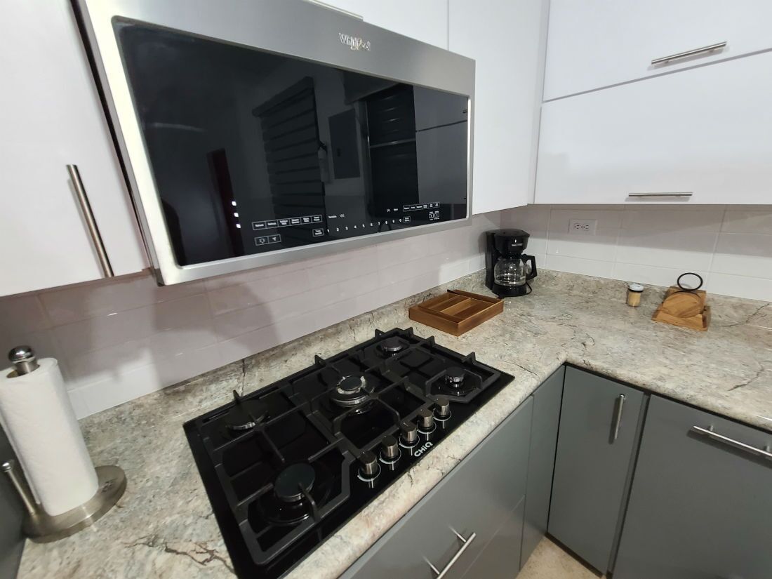A modern kitchen with a built-in stove, a coffee maker, and a large window above the counter.