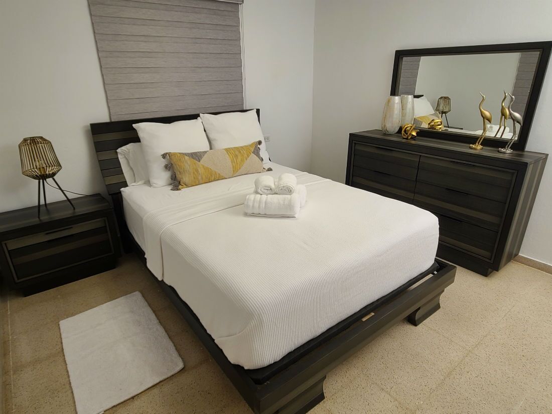 Un dormitorio ordenado con cama, cómoda, mesita de noche y espejo.