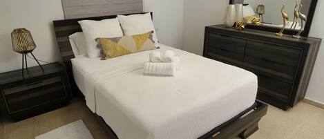 Un dormitorio ordenado con cama, cómoda, mesita de noche y espejo.