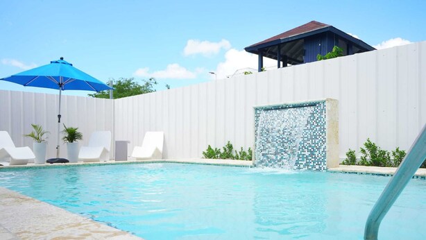 Ein Schwimmbecken mit Mosaikwand, Liegestühlen und einem blauen Sonnenschirm.