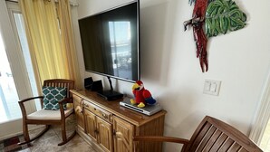 Una sala de estar con televisor, muebles de madera y un loro decorativo en la pared.