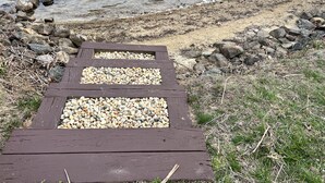 Un sendero de madera que conduce a una zona de guijarros junto a una masa de agua.