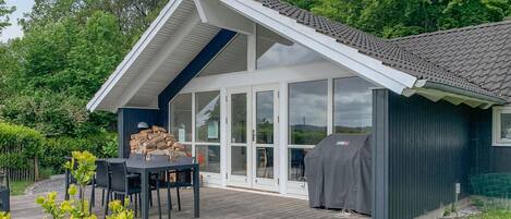 A modern house with a deck, a barbecue grill, and a covered outdoor seating area.