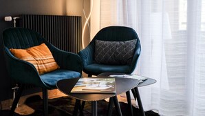 Une pièce moderne avec deux fauteuils bleu-vert foncé, l’un agrémenté d’un coussin à carreaux orange et l’autre d’un coussin à motifs noir et blanc. Une petite table noire, sur laquelle repose un magazine, se trouve devant les fauteuils.