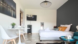 Une chambre d’hôtel moderne équipée d’un lit, d’une table à manger avec des chaises, d’un téléviseur et d’une petite table de chevet avec une lampe.