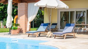A poolside area with lounge chairs, a white umbrella, and a brick wall. - Stunning home in Fanzolo di Vedelago (Fanzolo di Vedelago)