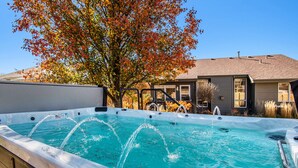 A hot tub with water jets, surrounded by a wooden deck and a house with a sloped roof.