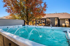 Un jacuzzi con chorros de agua, rodeado por una terraza de madera y una casa con techo inclinado.