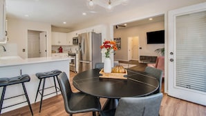A modern kitchen with white cabinets, a black dining table with four chairs, and a decorative vase with flowers.