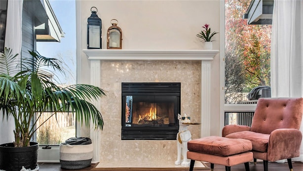 A cozy living room with a fireplace, a plush armchair, and a potted plant.