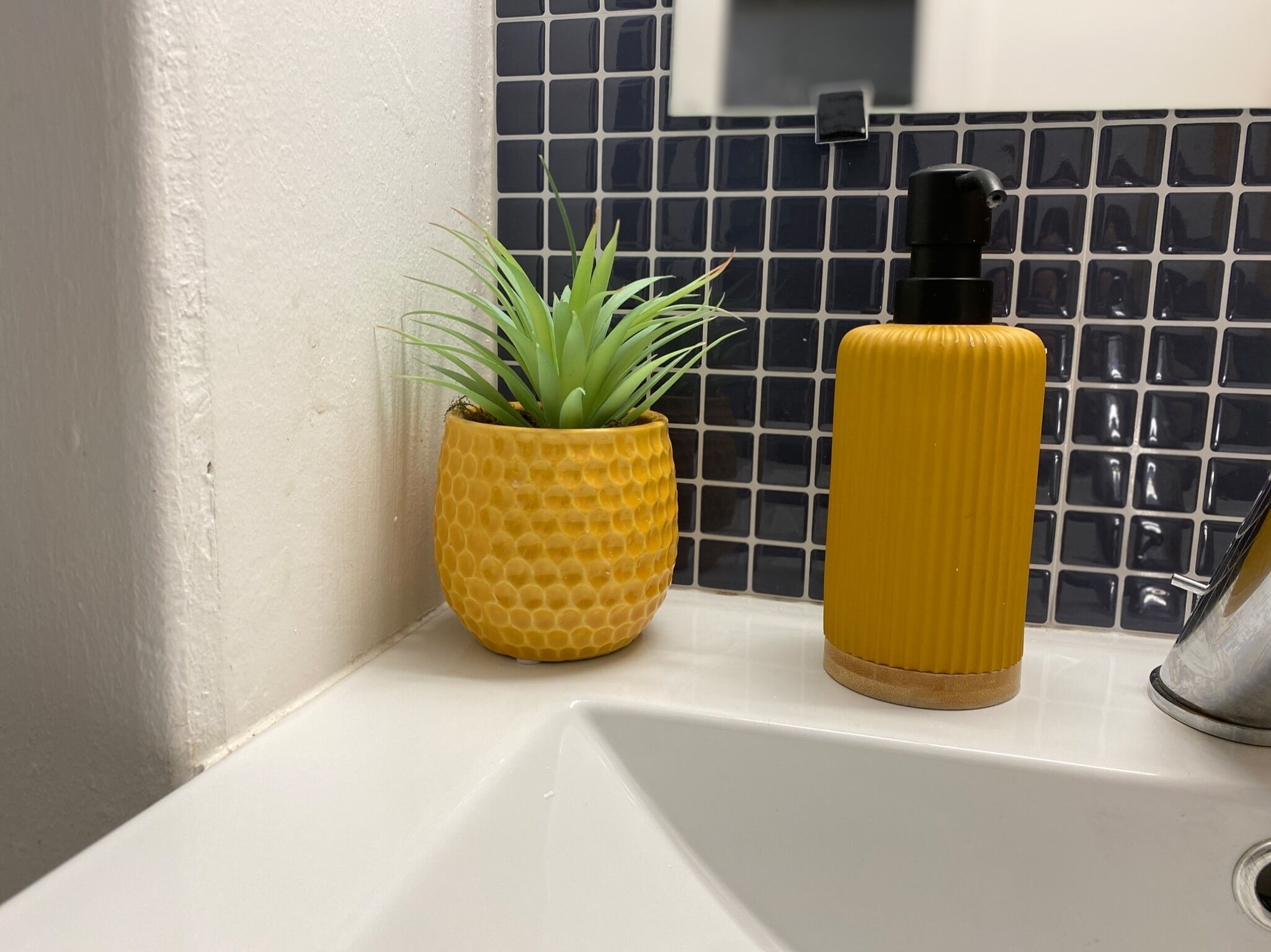 A bathroom sink with a yellow textured planter and a black bottle.