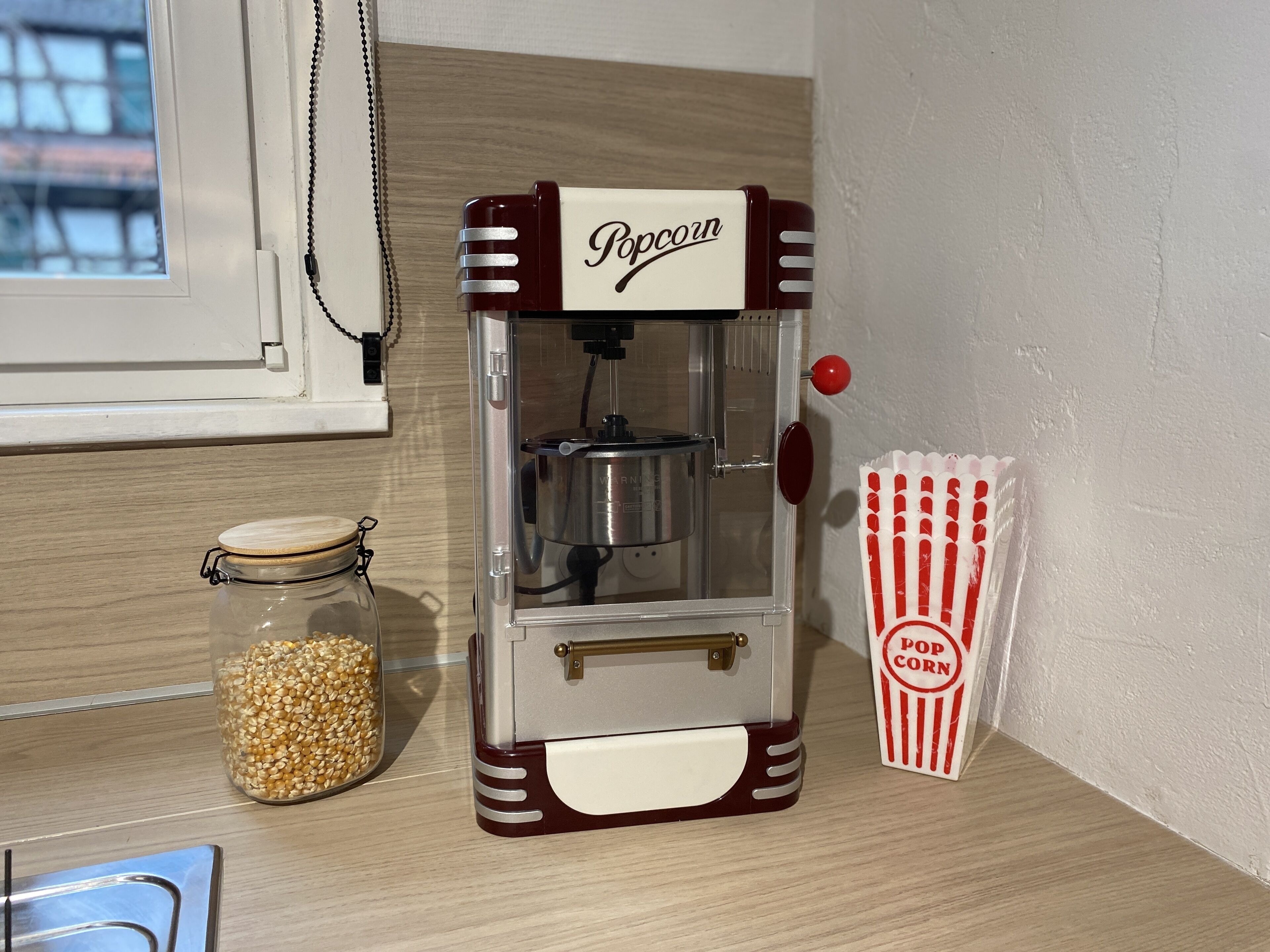 A popcorn machine with a jar of popcorn kernels and a popcorn bag on a wooden surface.