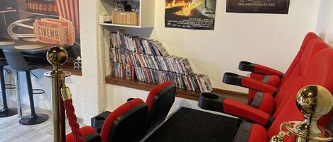 A cinema room with red seats, a popcorn stand, a DVD collection, and movie posters.