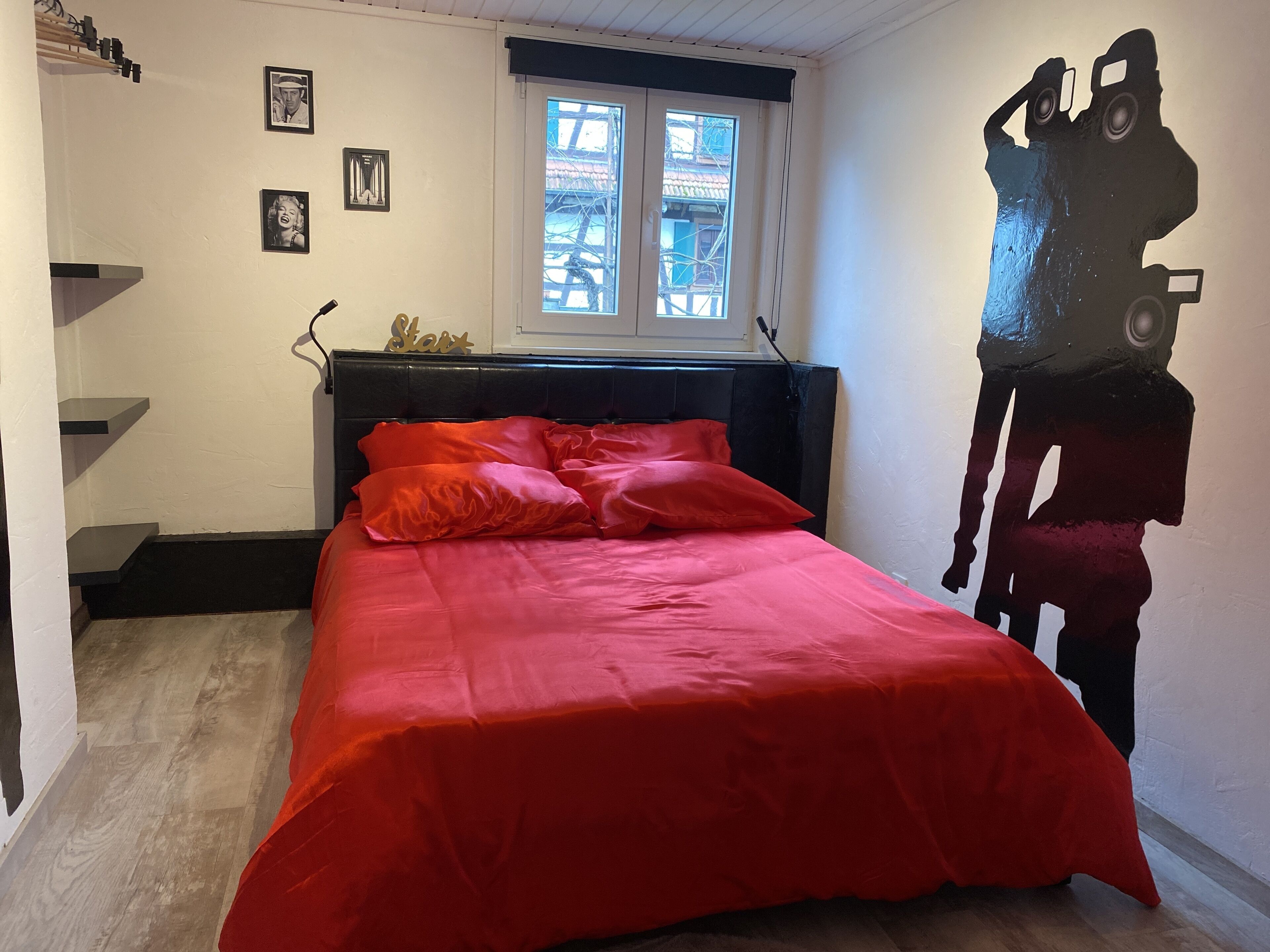 A bedroom with a bed, a window, and a wall with a large abstract painting.