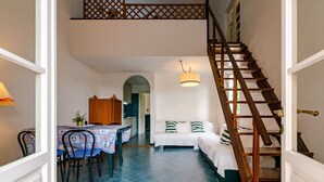 Quarto com cama, mesa e cadeiras, escada e área de cozinha.