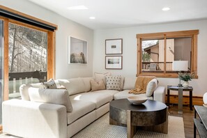 Una sala de estar con un sofá modular, una mesa de centro redonda y un ventanal con vistas a árboles.