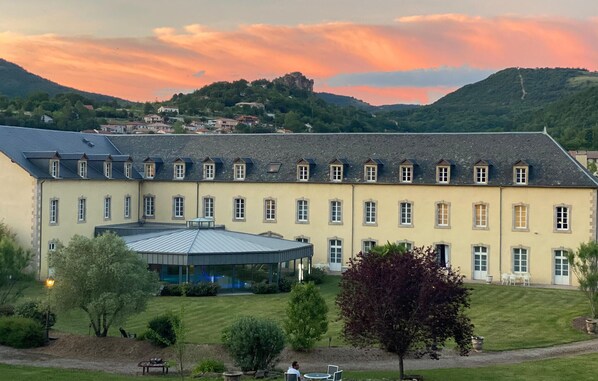 Ein großes, mehrgeschossiges Gebäude mit einer symmetrischen Fassade, einer überdachten Terrasse und einem gepflegten Rasen.