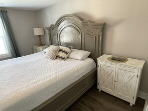 Restful retreat with a large bed, ornate headboard, and a nightstand with a lamp and cabinet.