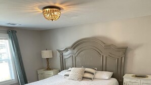A bedroom with a large bed, a nightstand, a lamp, and a wardrobe. - Karine's Cottage Beautiful Cottage w/ Boat Parking (Iuka)