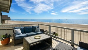 A balcony with wicker furniture, a potted plant, and a view of the beach and ocean. - Beachfront Bliss in Beautiful Carpinteria (Carpinteria)