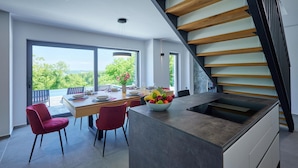A modern kitchen with a central island, a dining area with a view, and a staircase with wooden steps. - Nice home in Bedenica (Bedenica)