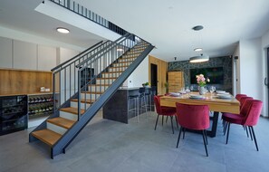 A modern kitchen with a built-in wine cooler, a dining area with a wooden table and red chairs, and a staircase with a metal railing. - Beautiful home in Bedenica with private swimming pool, can be inside or outside (Bedenica)