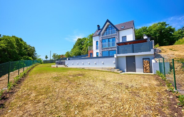 Ein modernes, zweistöckiges Haus mit großem Balkon, umzäunter Garten und blauem Himmel.