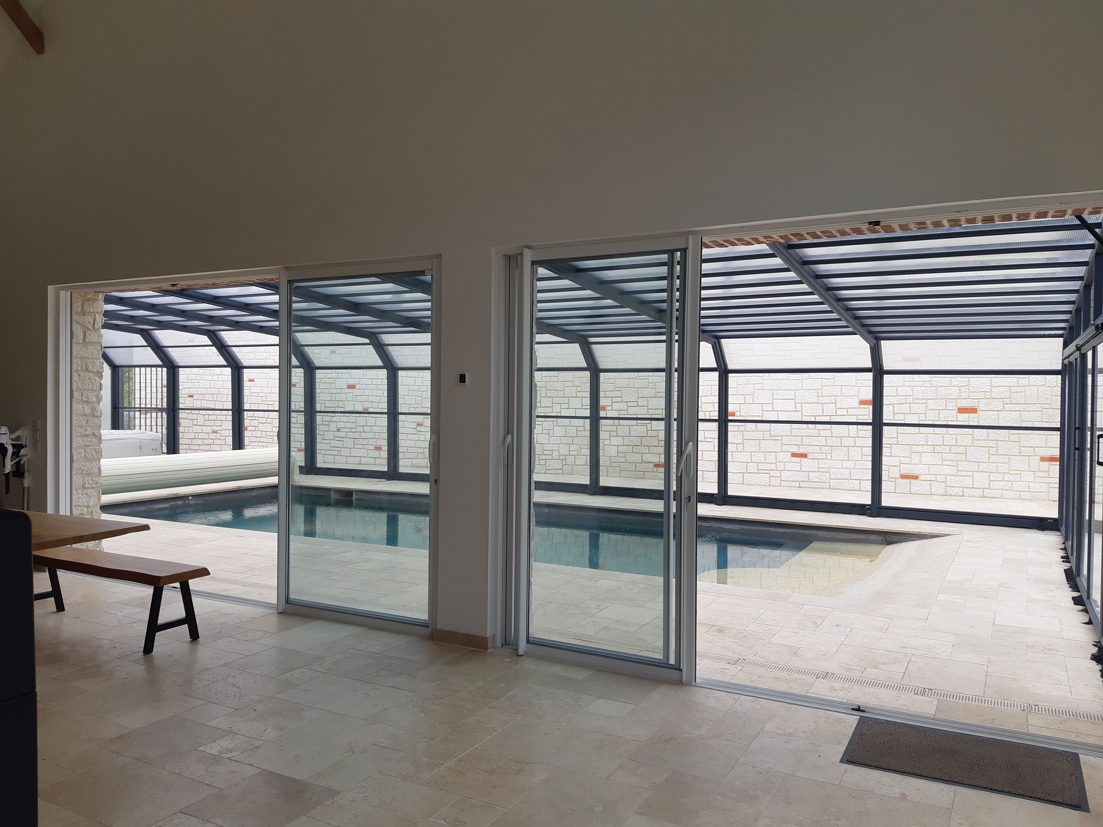Un espace intérieur spacieux avec une piscine, de grandes portes-fenêtres coulissantes et un banc.