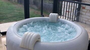 Ein Whirlpool mit zwei integrierten Sitzplätzen, umgeben von einer Glaskonstruktion mit Blick auf eine Rasenfläche und eine Backsteinmauer.