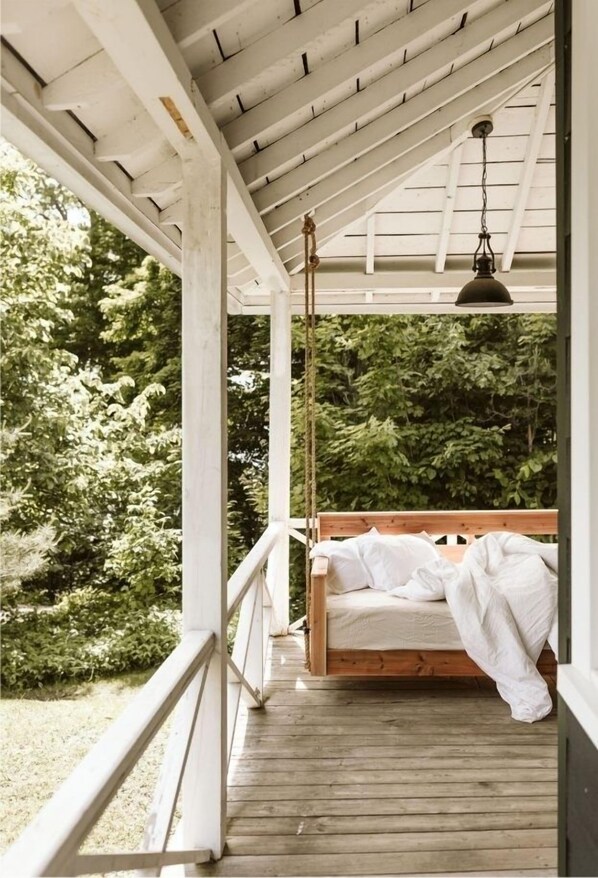 A wooden porch with a swing bed, white railings, and a hanging light fixture. - Charming Four Seasons Lake Front Renovated Cottage in Bala, Moon River Muskoka (Bala)