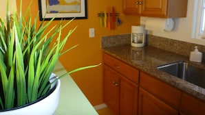A kitchen with wooden cabinets, a granite countertop, a coffee maker, and a potted plant.
