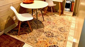 A compact kitchen with a dining area, featuring a white table, two chairs, a small rug, and a wooden wall.