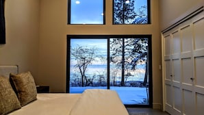 A bedroom with a large bed, a view of trees and a body of water through a sliding door, and a white wardrobe. - Skipping Stone Lake House, Skipping Stone Lake House (Woods Bay)