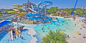 A water park with multiple slides and pools, surrounded by beach areas with sun loungers. - Private River Access, Pool, Hot tub, BBQ grill walk downtown & Bahn. Free Tubes! (New Braunfels)