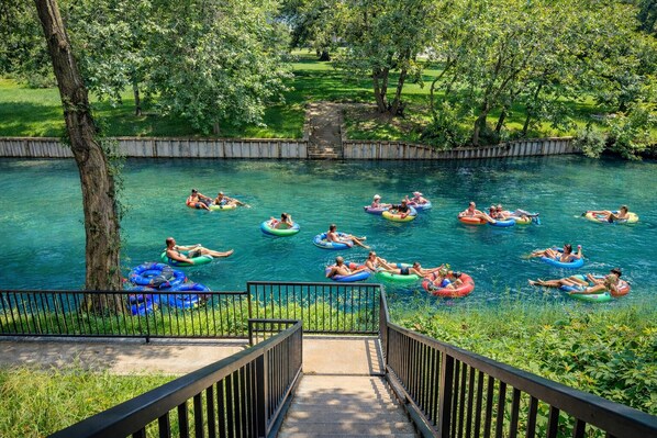 A river with people on inflatable tubes, surrounded by greenery and a stone structure. - Private River Access, Pool, Hot tub, BBQ grill walk downtown & Bahn. Free Tubes! (New Braunfels)
