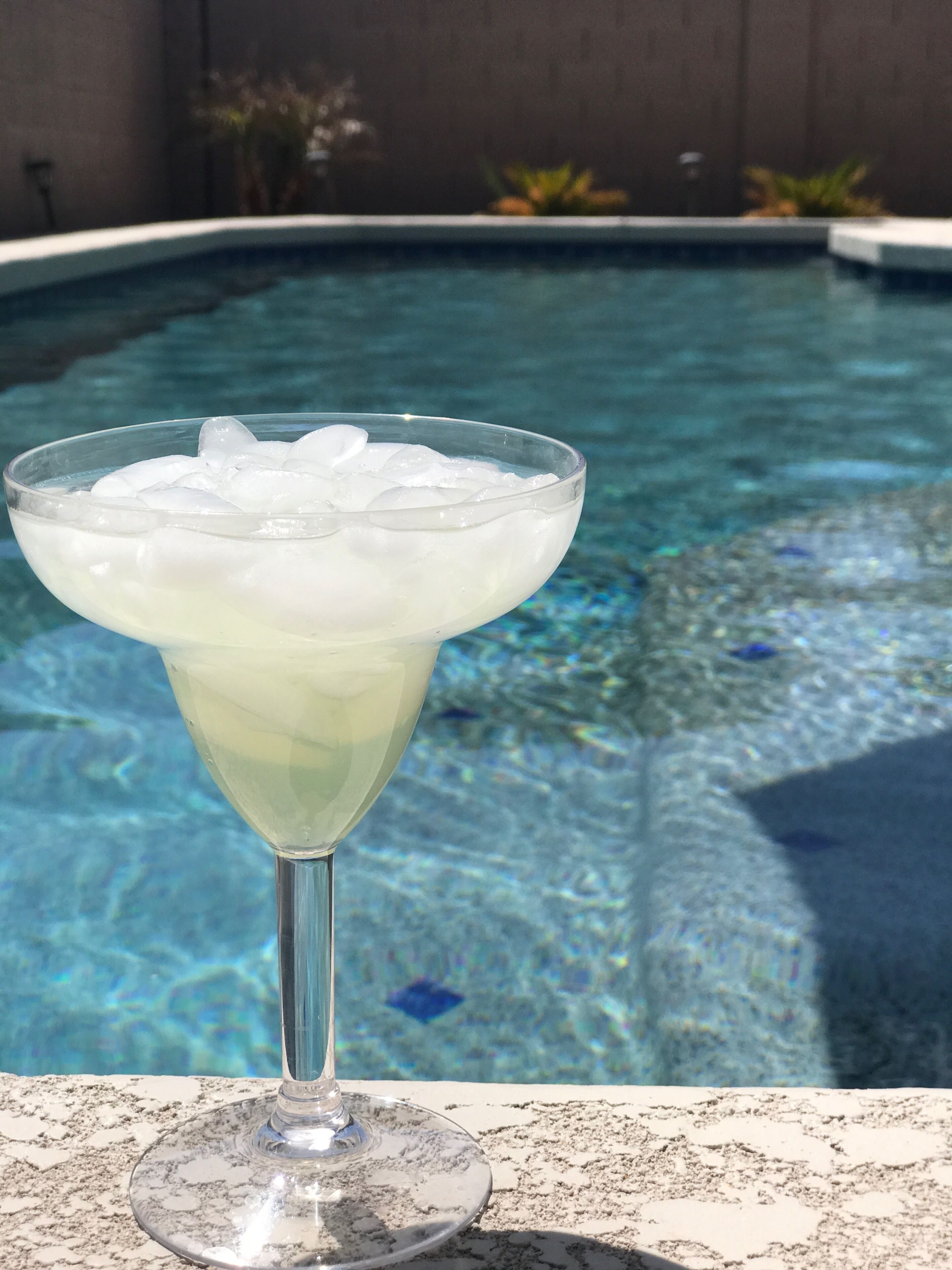 A cocktail glass with ice cubes on a poolside table.