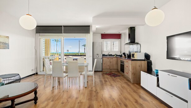 A modern kitchen with white cabinets, a dining area with a wooden table and chairs, and a large window with a view of the beach. - WELCS APARTAMENTO 218 EMP frente al Mar (Empuriabrava)