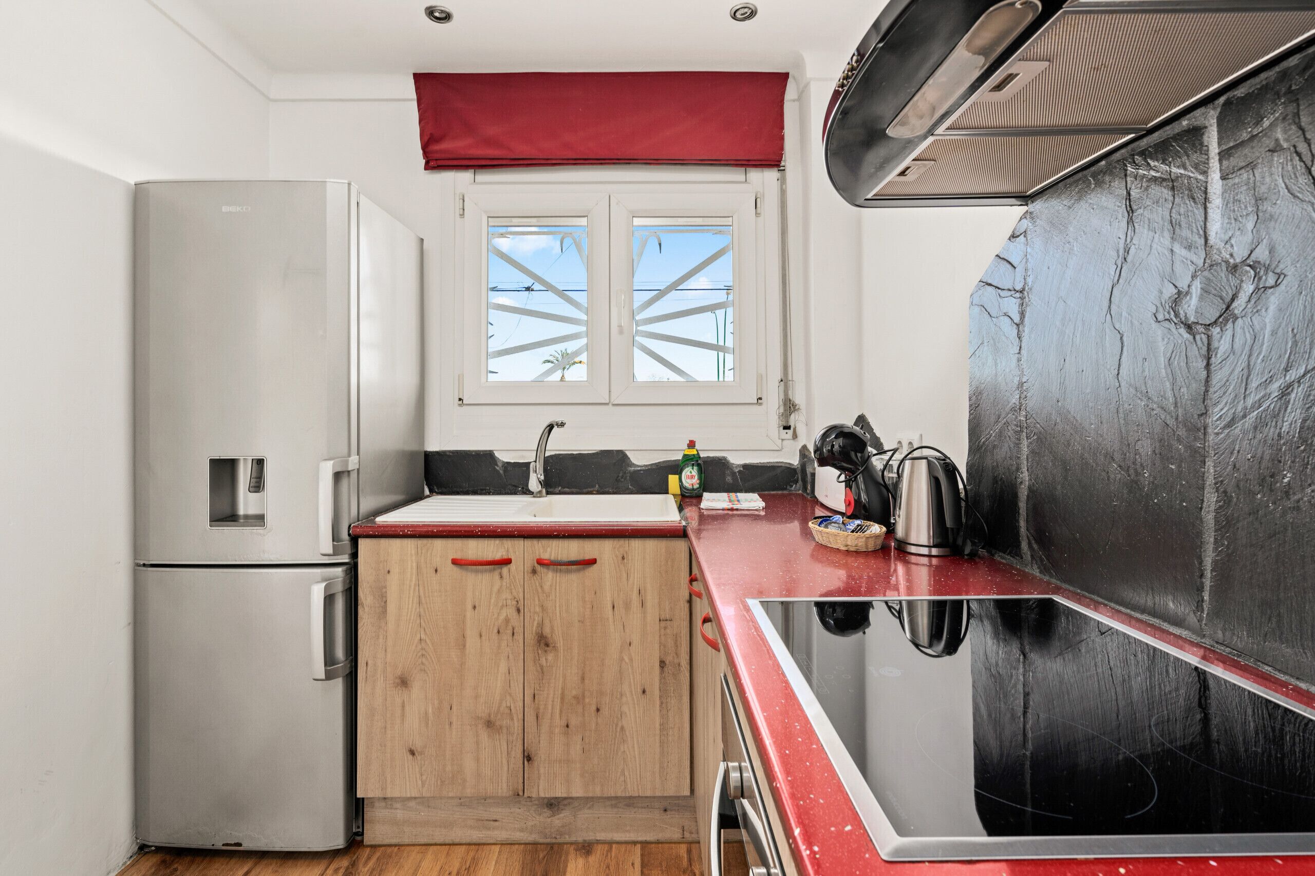 A compact kitchen with a refrigerator, wooden cabinets, a sink, and a stove.