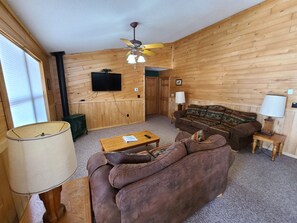 Ein gemütliches Wohnzimmer mit Holzwänden, einem Deckenventilator, einem Fernseher, einer Couch und einem Couchtisch.