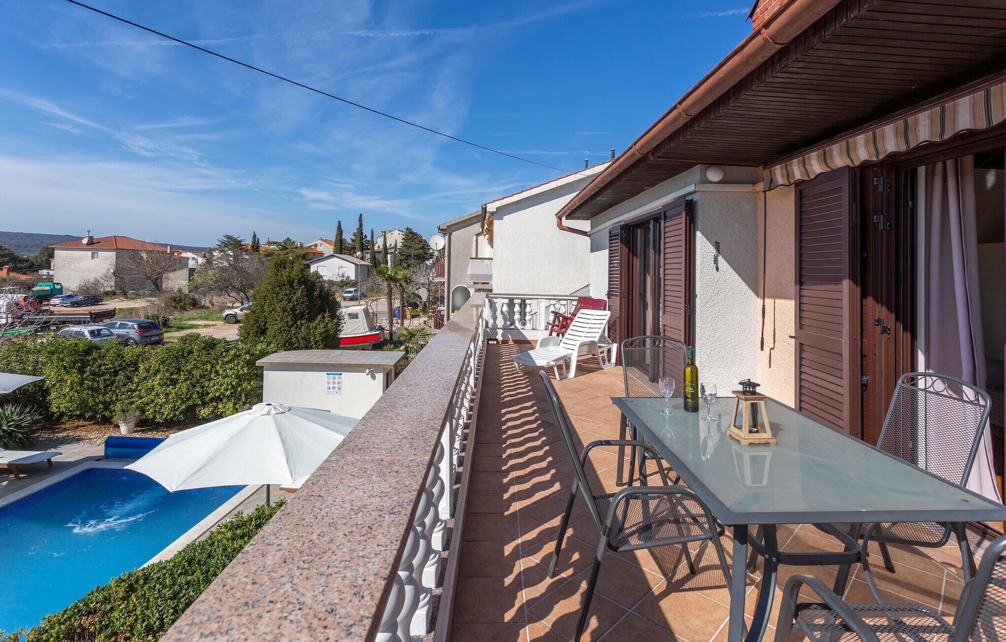 A balcony with a pool, outdoor seating, and a view of the surrounding area.