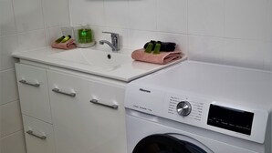 A modern laundry room with a white washing machine, a sink, and a cabinet with drawers.
