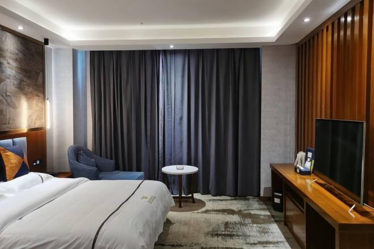 A hotel room with a bed, a desk, a chair, a small round table, and a large window with curtains.