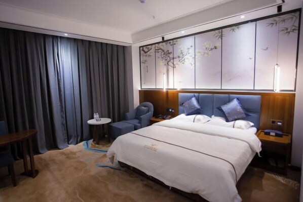 A modern hotel room with a large bed, a seating area with a small table, and a decorative wall panel.
