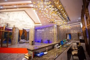 A modern hotel lobby with a reception desk, seating area, and a decorative wall with hanging elements. - Jingan Haoting Hotel (Gengma)