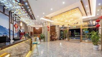 A hotel lobby with a reception desk, seating area, and a large chandelier.
