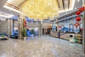 A hotel lobby with a marble floor, a reception desk, and a large chandelier.