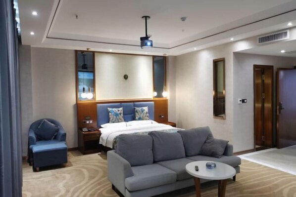 A modern hotel room with a large bed, a sofa, a small table, and a chair. There is a ceiling light and a door in the room. - Jingan Haoting Hotel (Gengma)